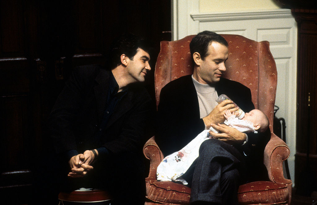 Tom Hanks feeds a baby while Antonio Banderas watches in a scene from the film 