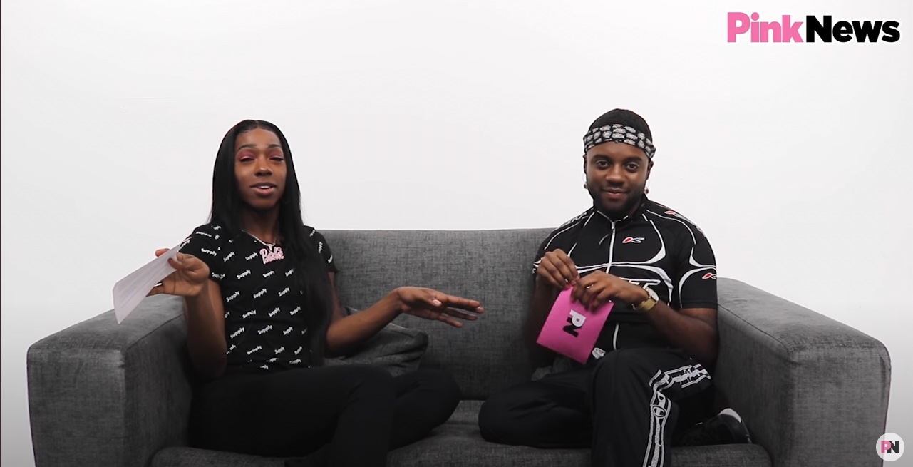 This is an image of two Black men sitting on a couch in a white room. 