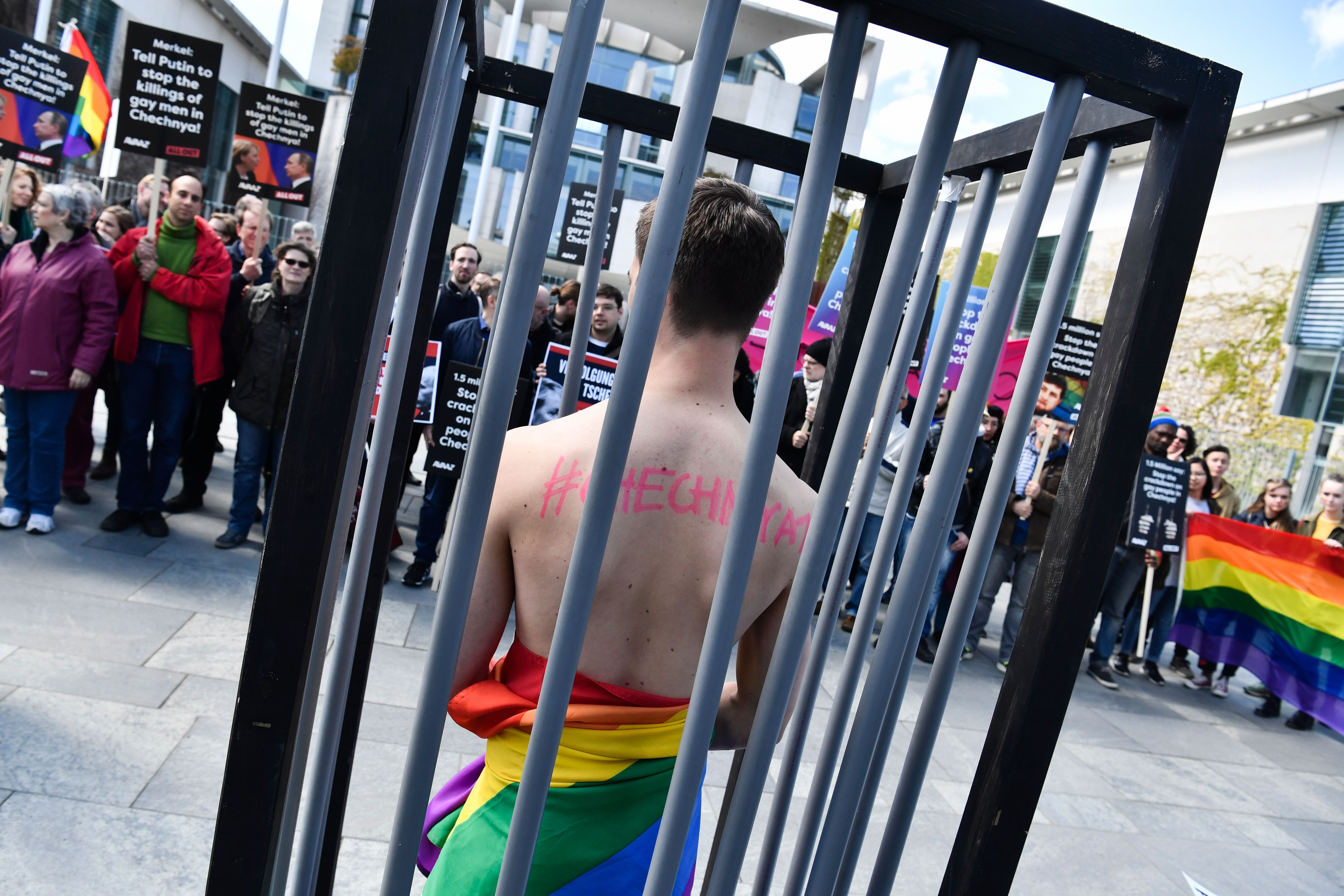 An activist stands naked, wrapped in a rainbow flag, in a mock cage in front of the Chancellery in Berlin on April 30, 2017, during a demonstration calling on Russian President to put an end to the persecution of gay men in Chechnya.