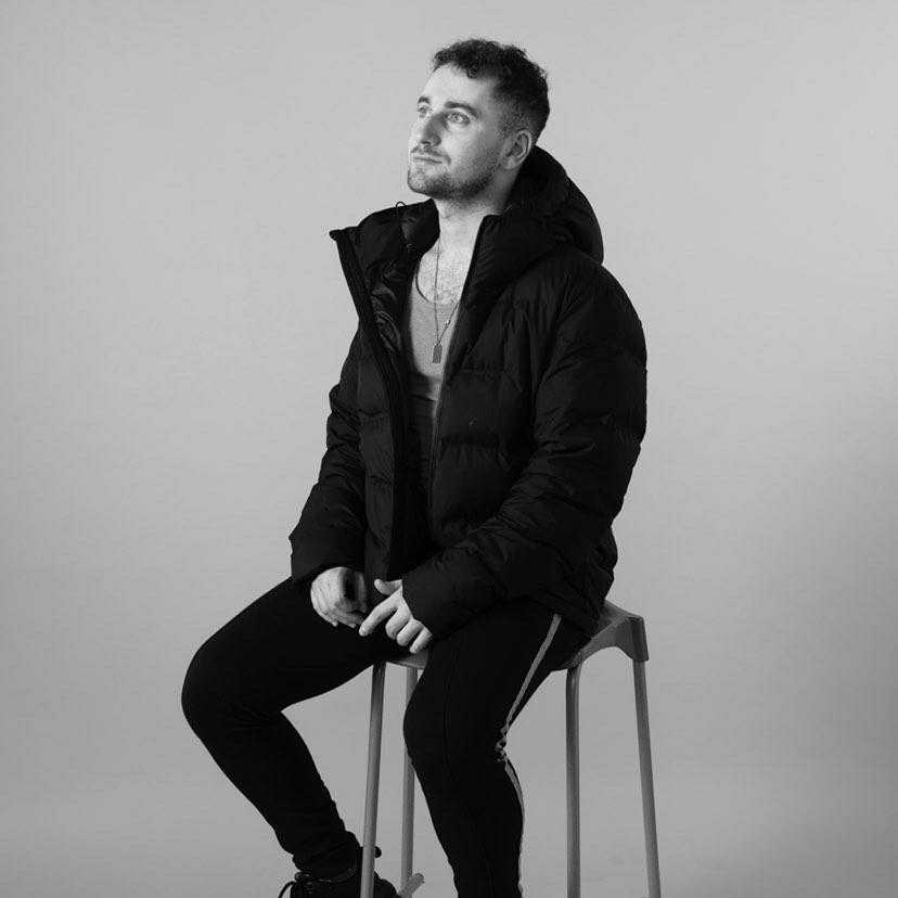 A black and white picture of Ciaron sitting on a stool