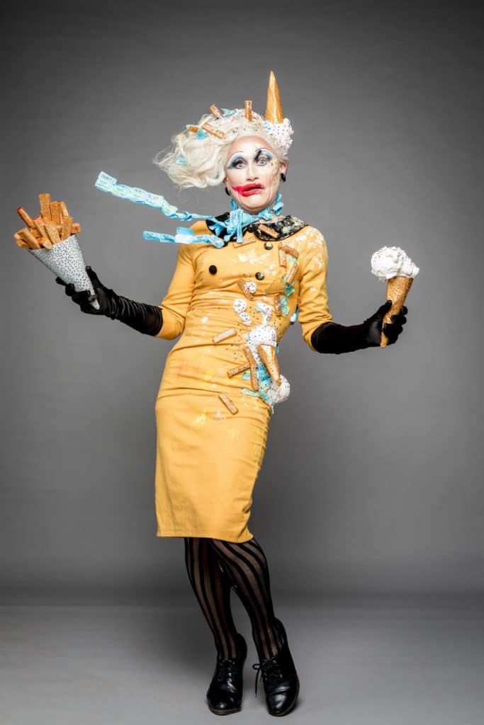 Joe Black with windswept hair, an iice cream cone on his head and ice cream splatters over his dress