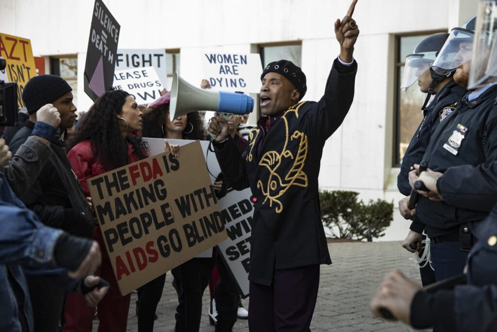 Blanca and Pray Tell at a protest, Pray is holding a megaphone and Blanca is holding a placard that reads 