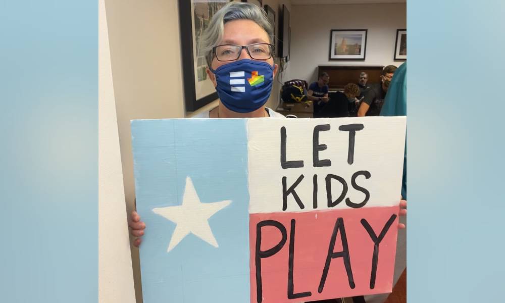 Picture of Hillary Moore-Embry who is a parent fighting anti-trans legislation in Texas, they hold up a sign that reads 