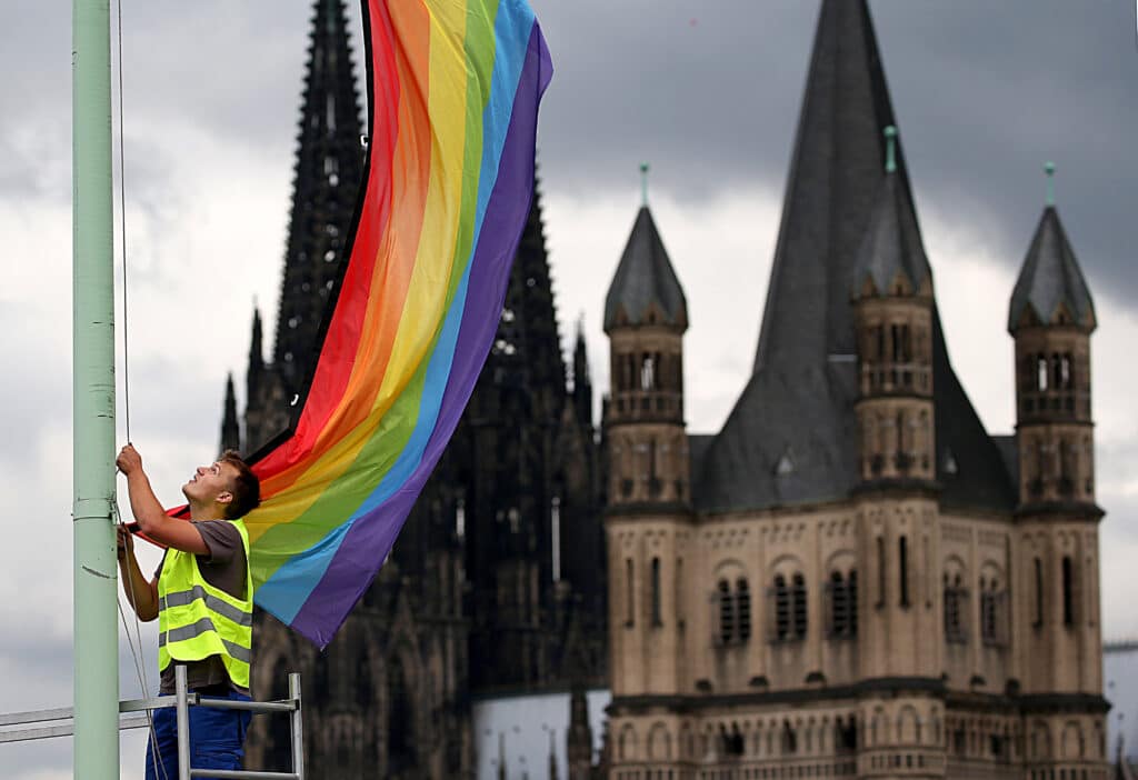 The Cologne Cathedral (L) and the church Gross St Martin (R) are seen in the background as a man hoists a rainbow flag