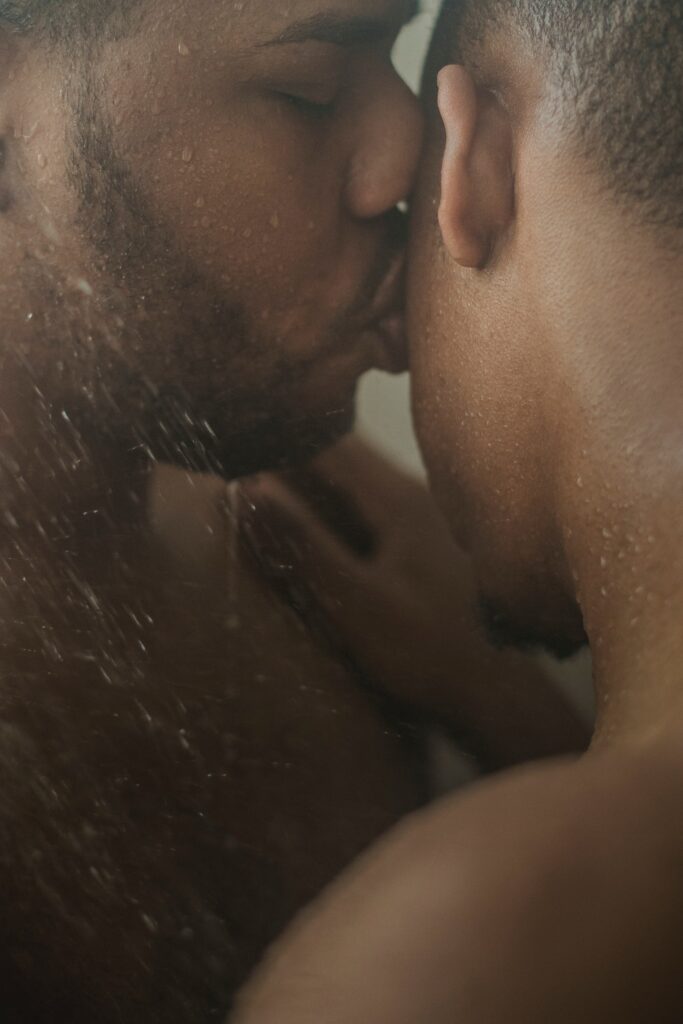 Two men kissing under a shower