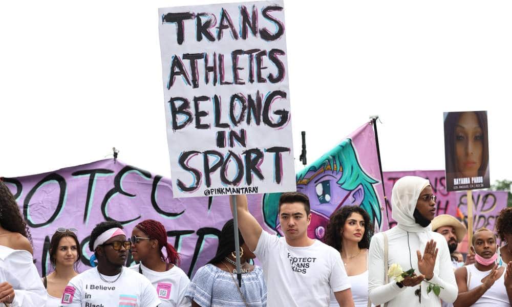 A person holds up a sign that reads &quot;Trans athletes belong in sports&quot; during a demonstration