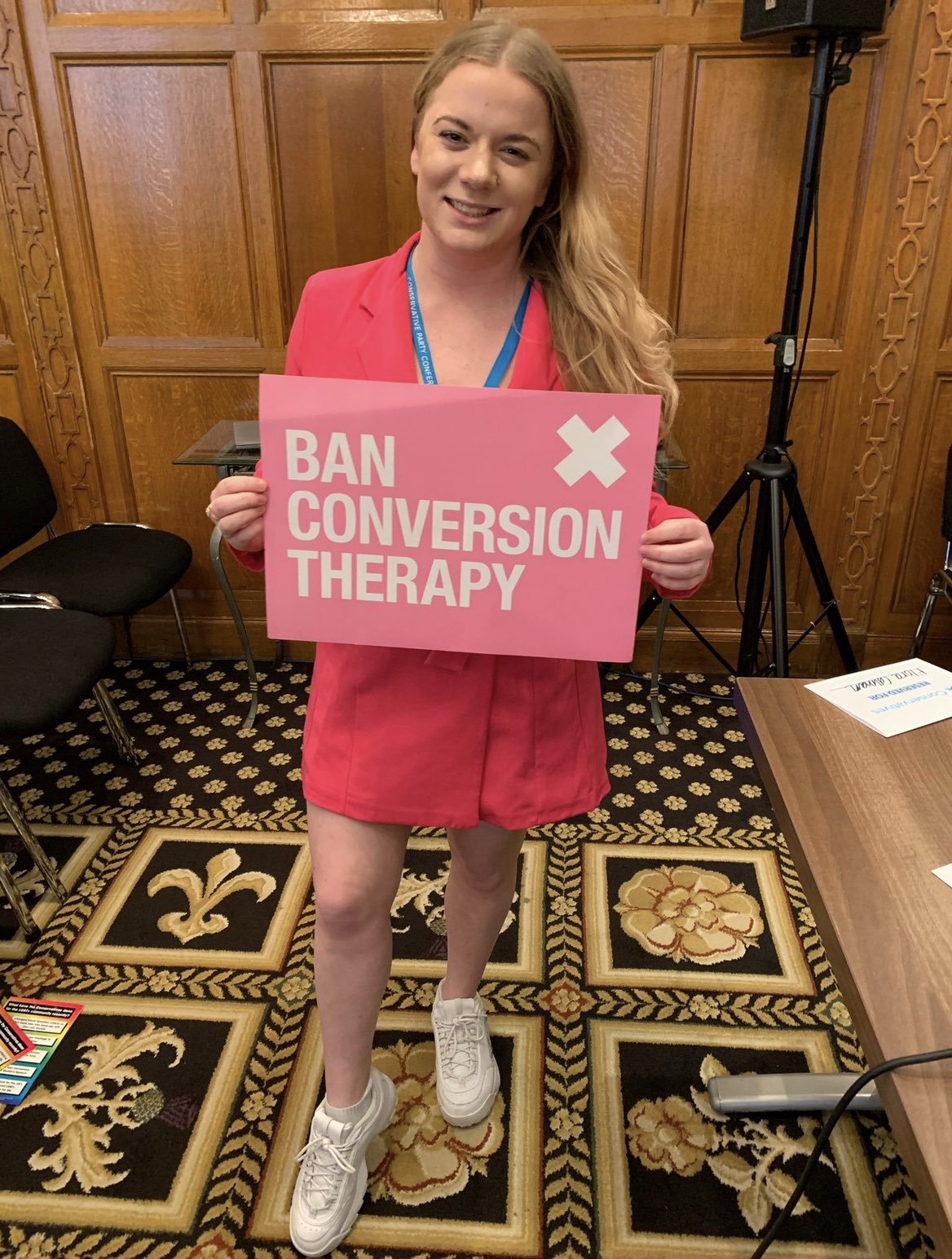 Elena Bunbury holding a sign that reads &quot;Ban Conversion Therapy&quot;. 