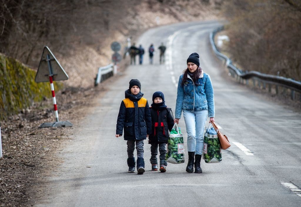 A woman with two children and carrying bags walk on a street to leave Ukraine.