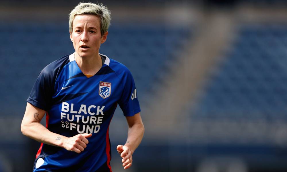 Megan Rapinoe wears a blue OL Reign jersey with the words &quot;Black Future Coop Fund&quot; written in white across her torso as she runs down the field