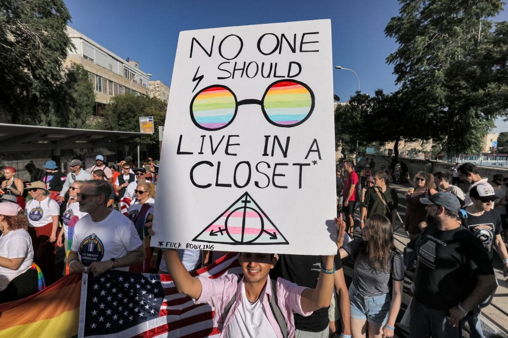 A Pride participant marches with a sign reading in English &quot;no one should live in a closet&quot;, with round, Harry-Potter style glasses with a rainbow motif and the deathly hallows symbol (also from Harry potter) in the colour of the trans pride flag.