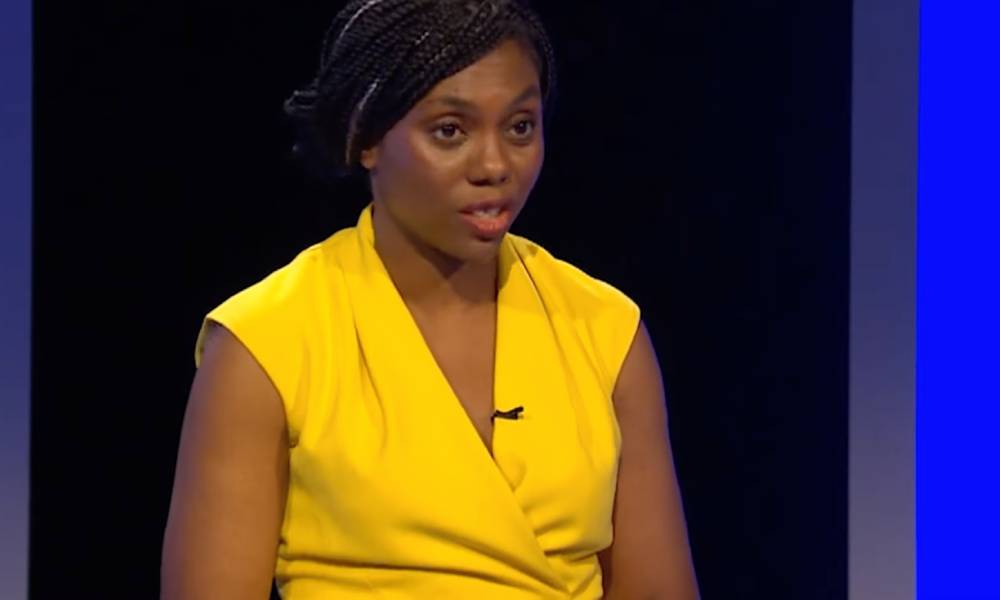 Kemi Badenoch wears a bright yellow outfit as she speaks at a podium during a Tory leadership election debate