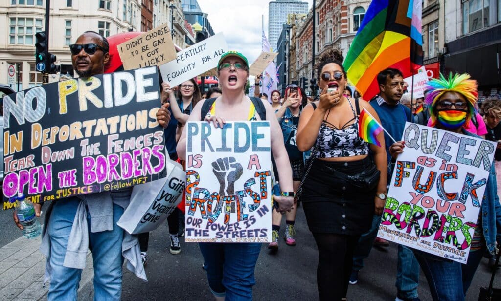 Several LGBTQ+ advocates gather in a crowd to protest against legislation that would imperil queer asylum seekers