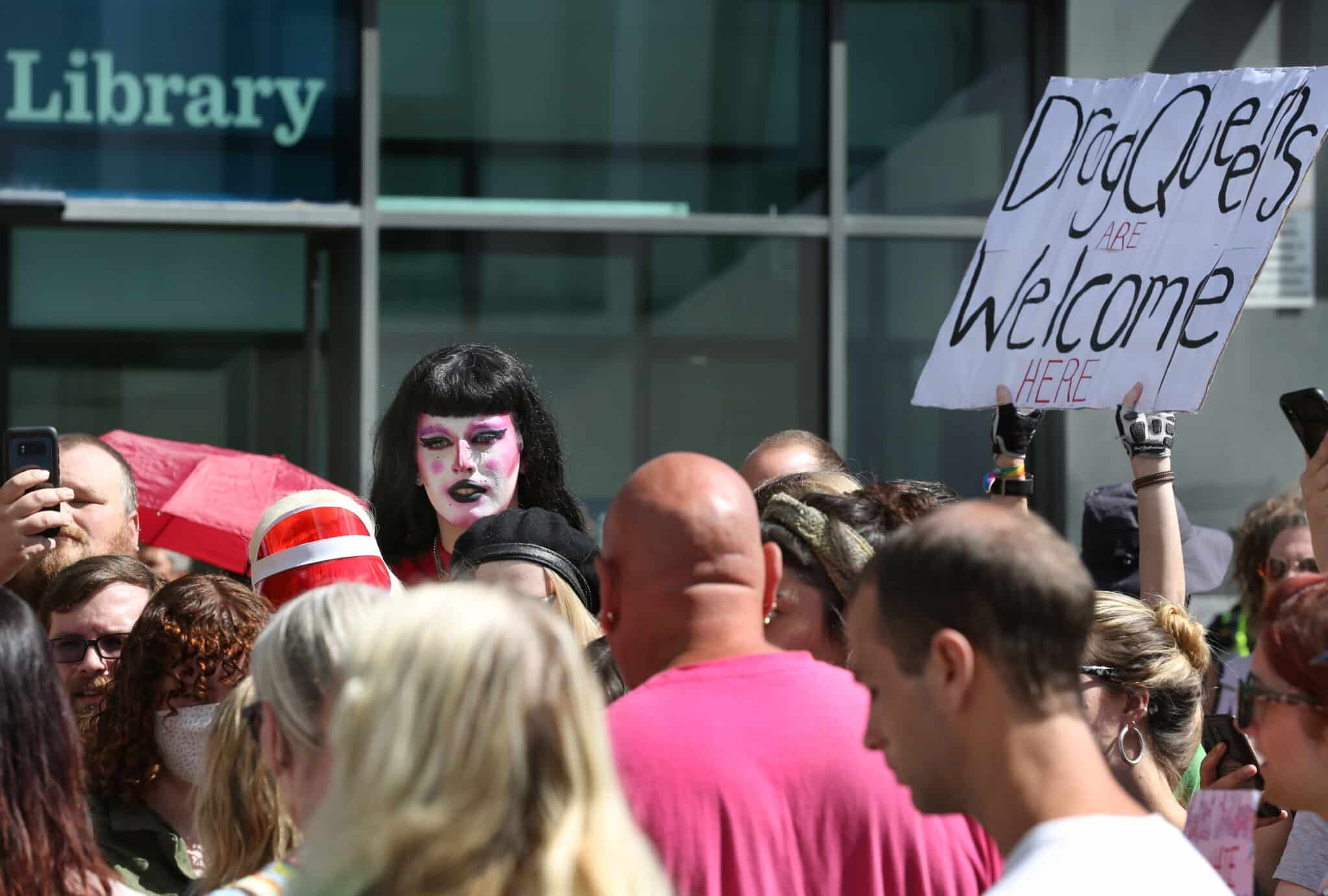 A crowd protesting against the exclusion of drag queens. One person holds a sign that says, &quot;Drag queens welcome here&quot;