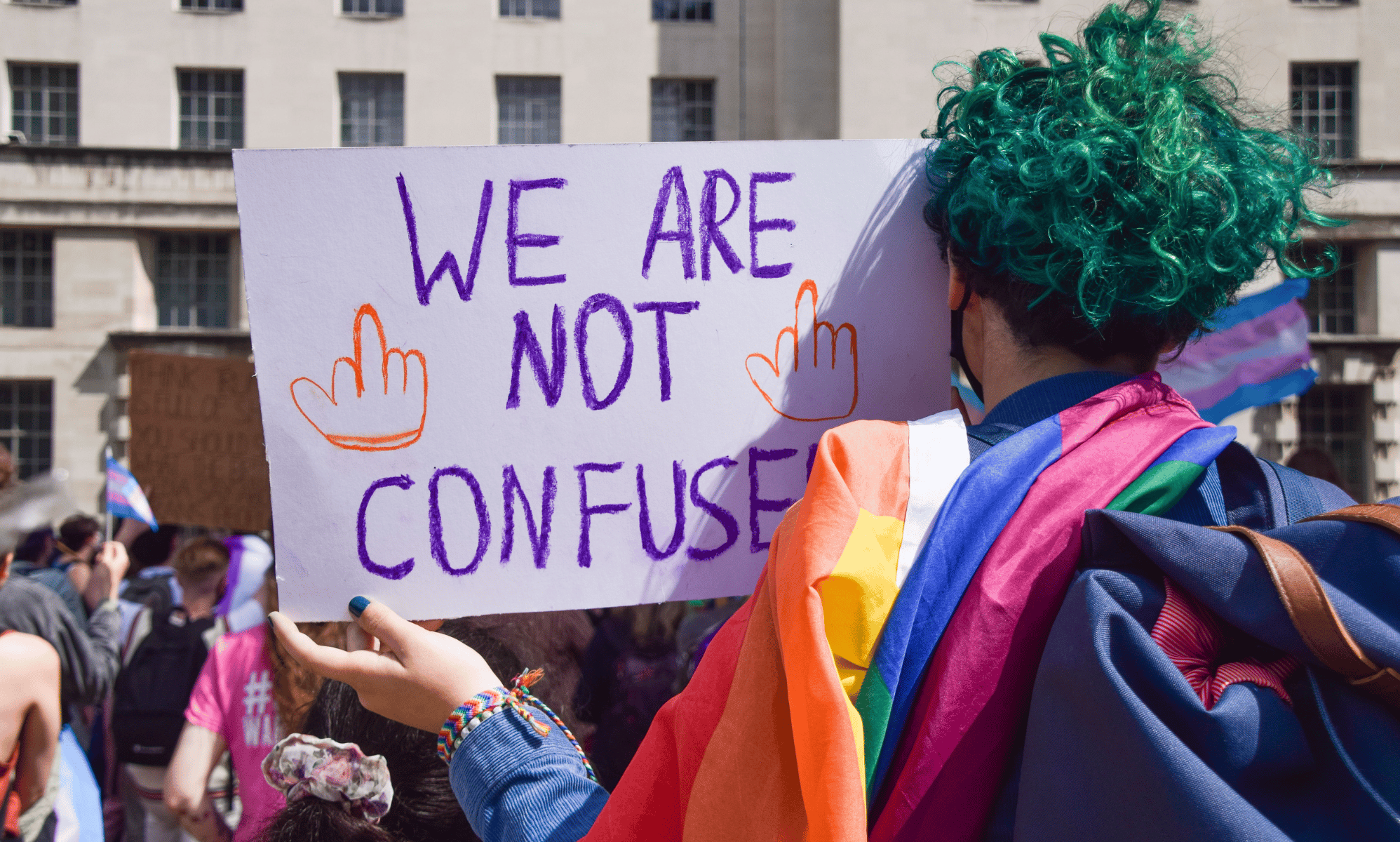 A person with green hair, who has their back turned to the camera, holds up a sign reading 