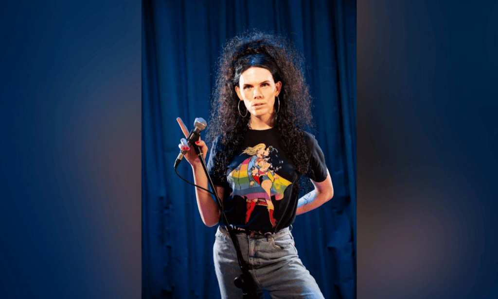 Jordan Gray holds a microphone as she stands in front of a blue curtain