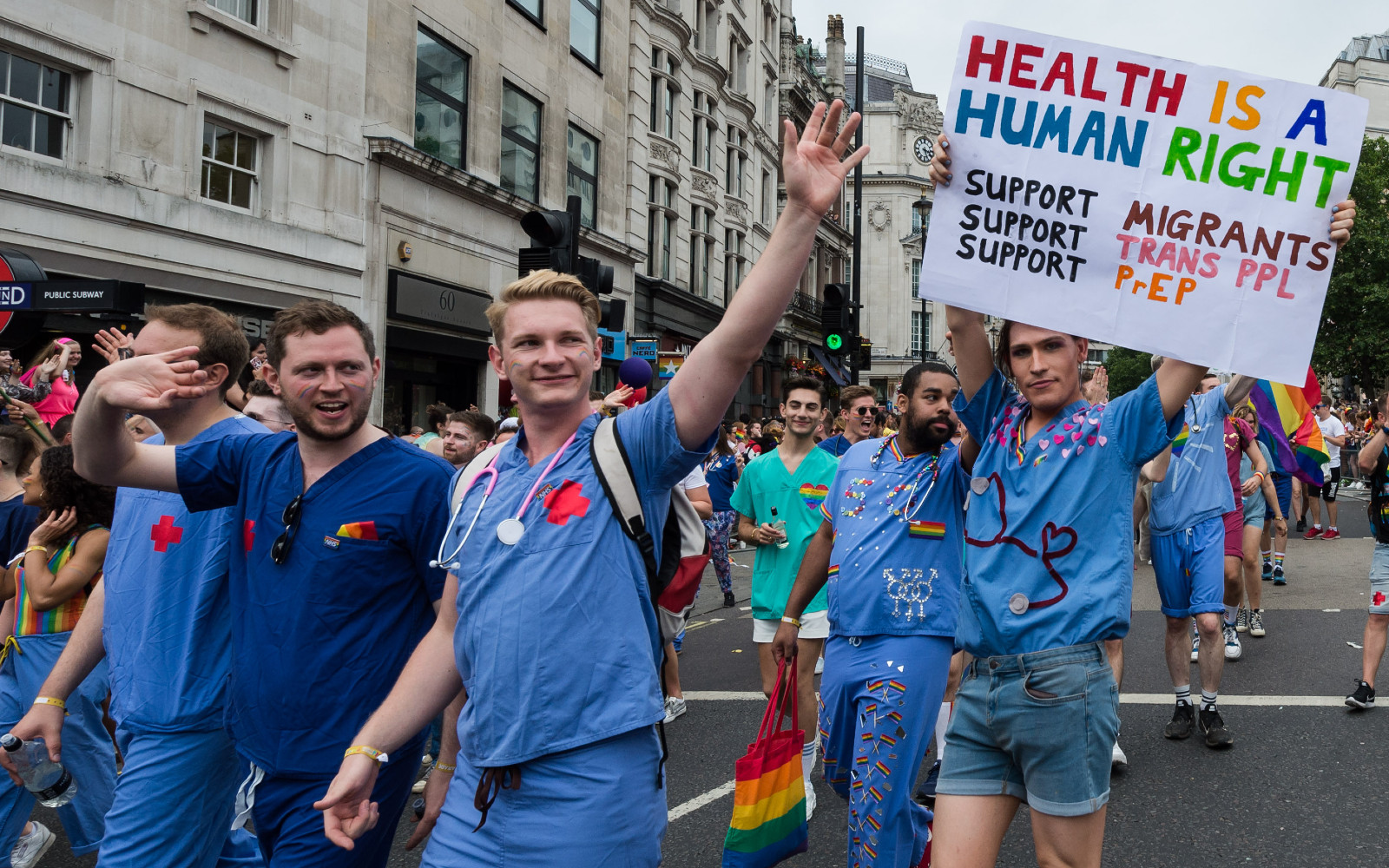 A group of NHS England doctors during a Pride parade. One is wearing a sign that reads: &quot;HEALTH IS A HUMAN RIGHT. Support Migrants, Support Trans PPL, Support PrEP&quot;