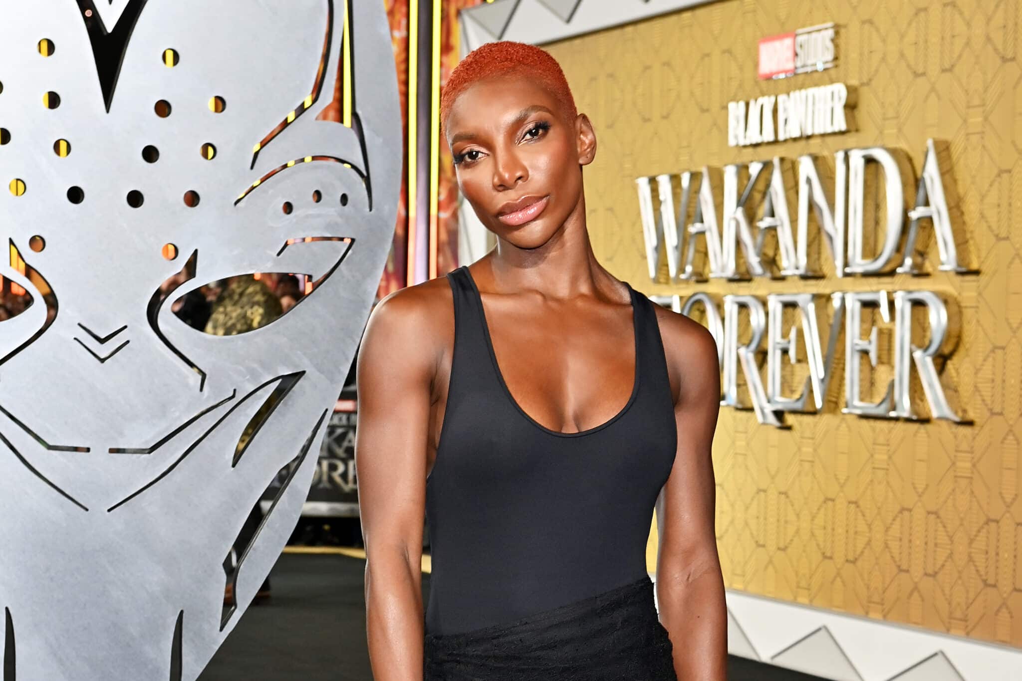 Michaela Coel posing bey an image of Black Panther