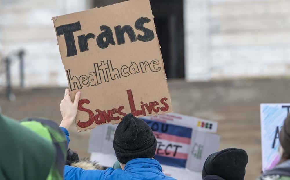 A trans rights protester holds a sign that reads: &quot;Trans healthcare saves lives.&quot;