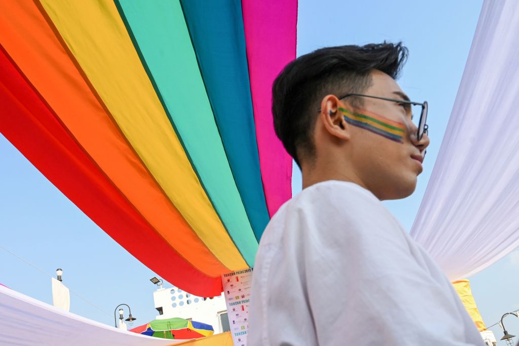 A member of the LGBTQ+ community stands under a rainbow flag displayed on a boat during the Pride Boat Parade, an event of the Myanmar