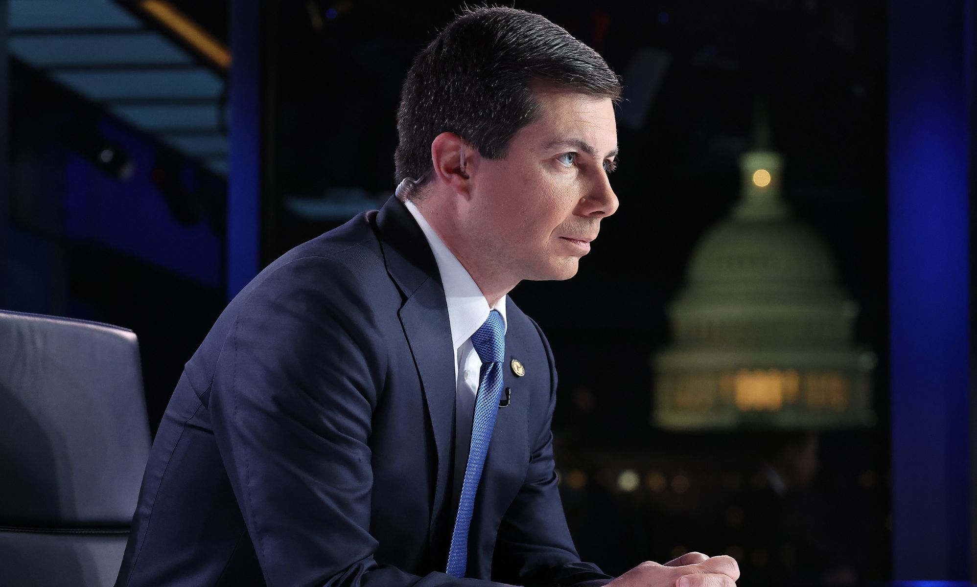 Pete Buttigieg, arched forward, sits during a Fox News broadcast while wearing a suit and blue tie.
