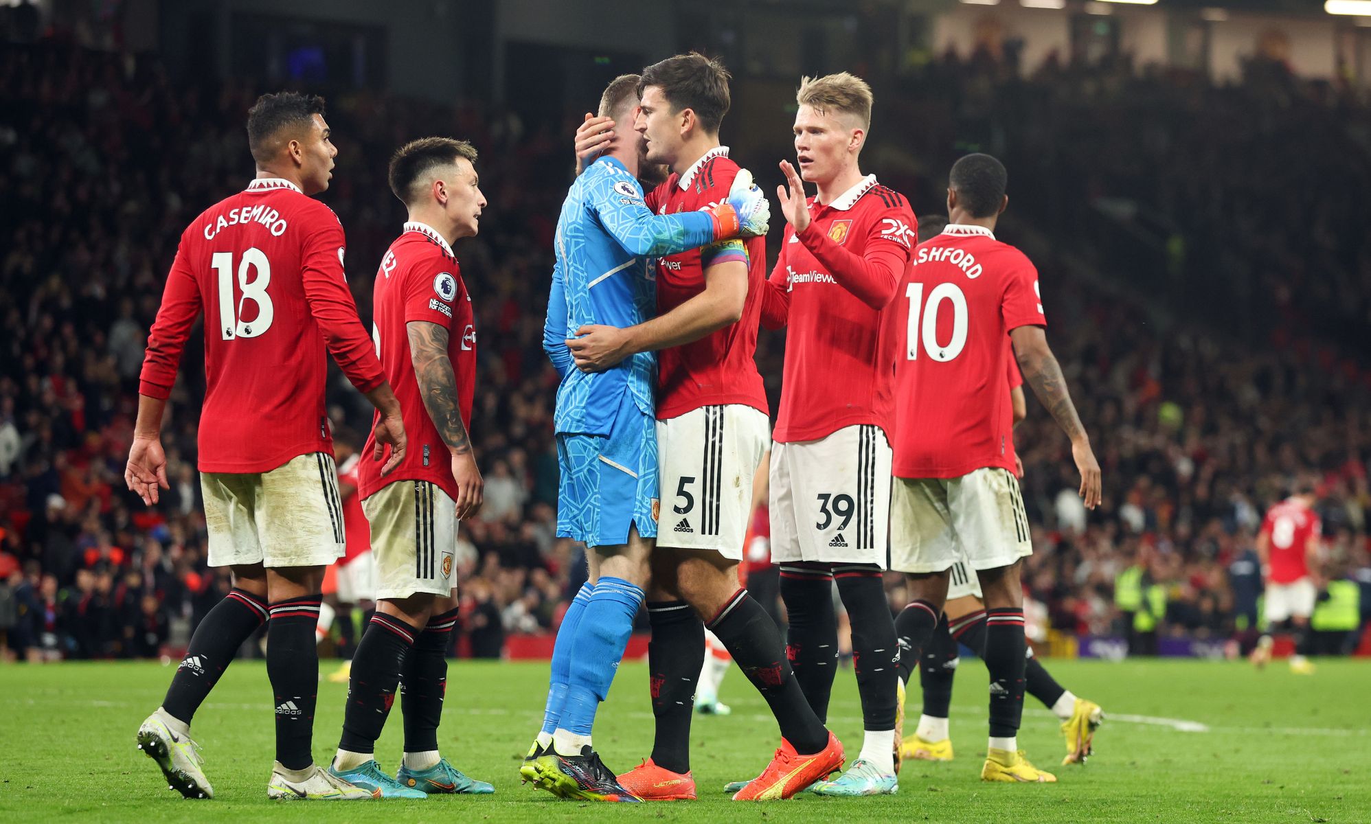 Manchester United players, wearing red football uniforms, gather around each other