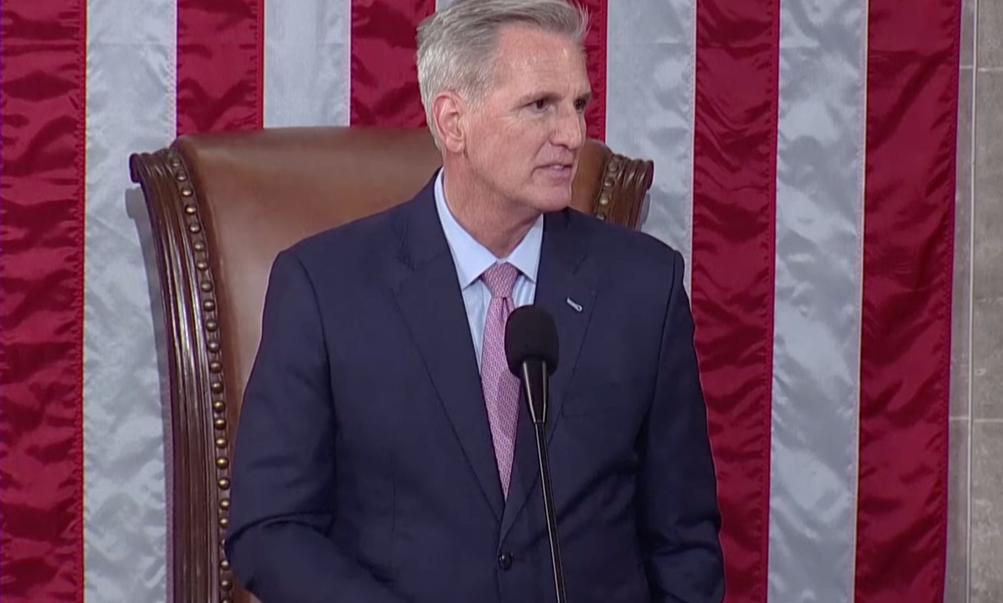 Republican congressman Kevin McCarthy, who is wearing a suit and tie, stands at a podium in front of the red, white and blue US flag as he