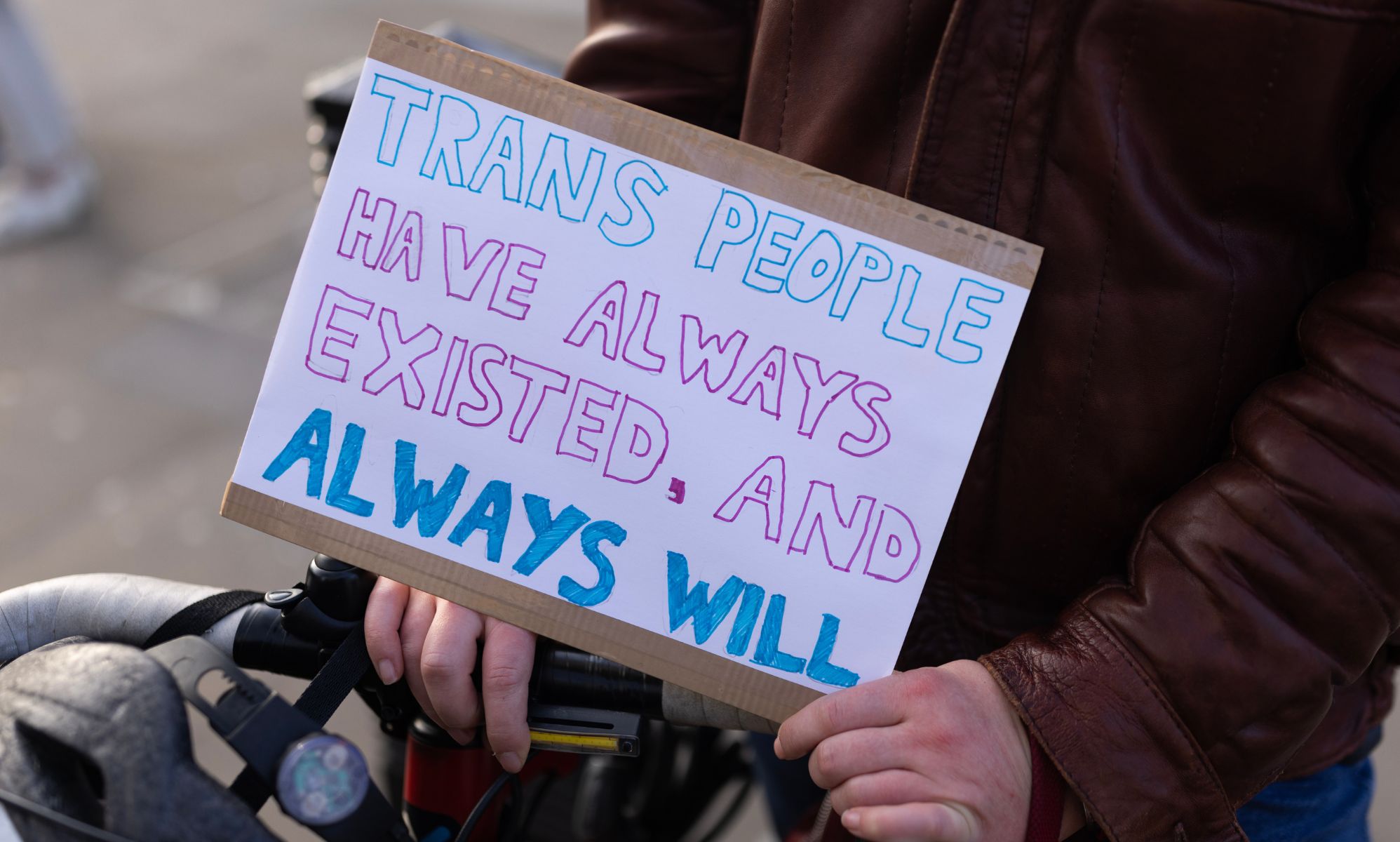 A person holds a sign saying &quot;trans people have always existed, and always will.&quot;