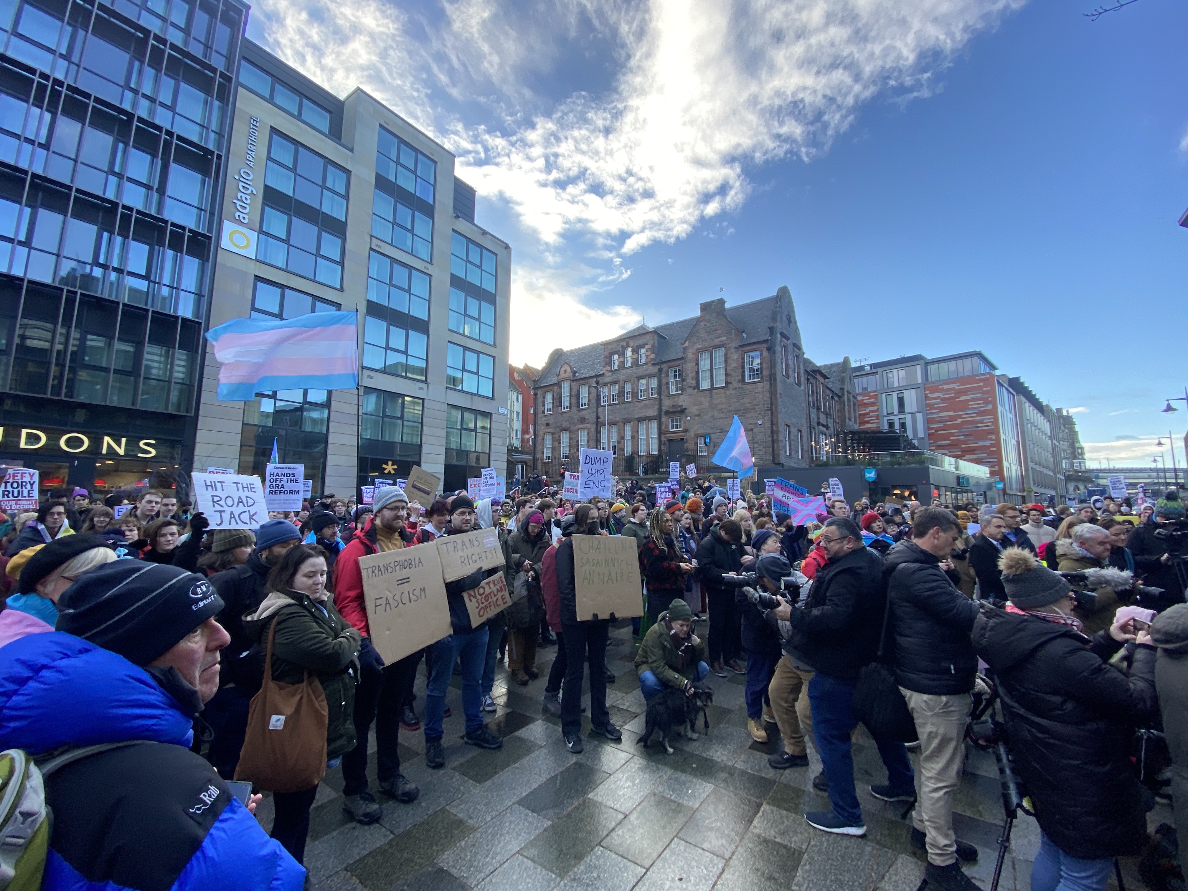 A photo shows trans activists standing in edinburgh for a trans rights rally. Some are holding signs