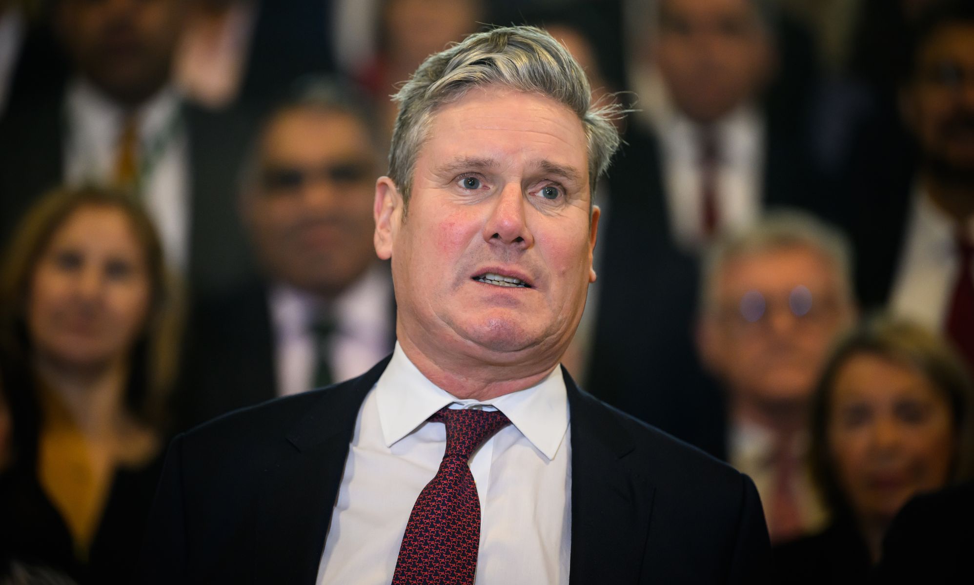 Keir Starmer, wearing a dark red tie, speaks in front of a group of people.