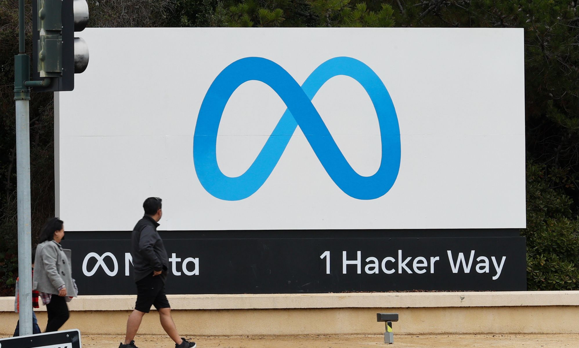 Individuals walk past the sign pointing towards Meta