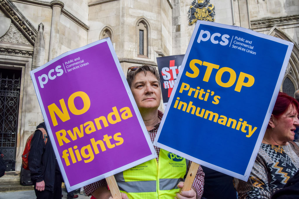 A protester holds placards opposed to the Rwanda refugee scheme during a demonstration in London. The signs read &quot;No Rwanda flights&quot; and &quot;Stop Priti