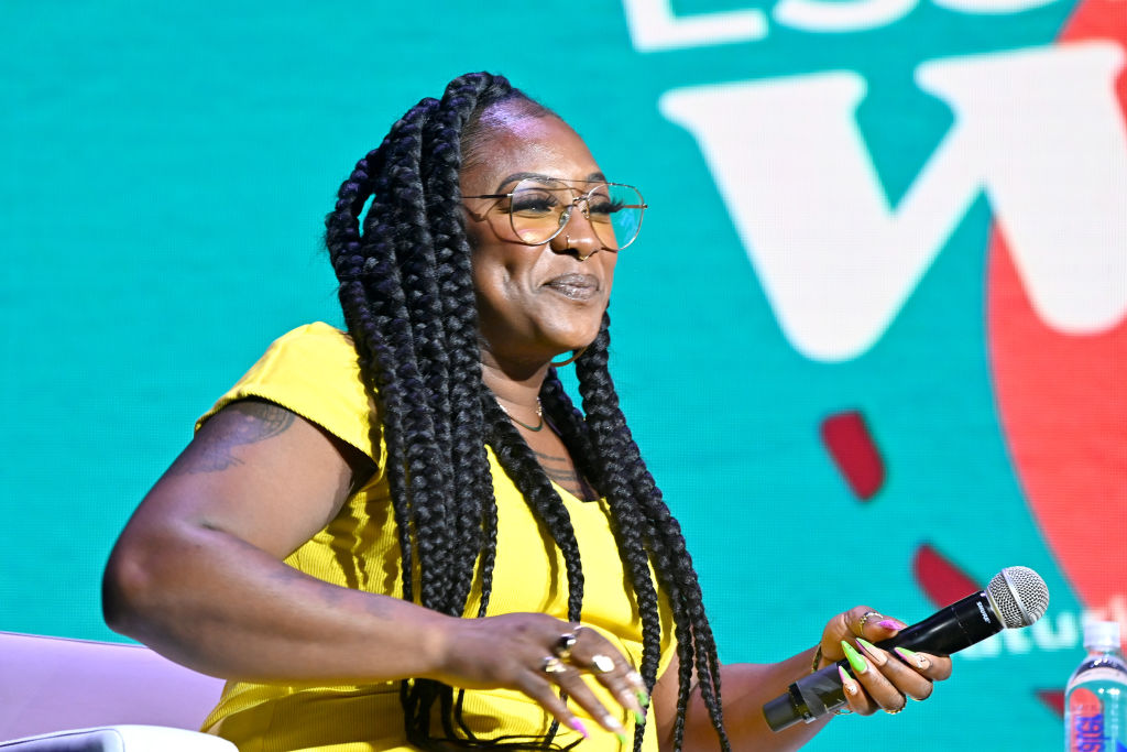 Wearing bright yellow, Alicia Garza is speaking at a panel.