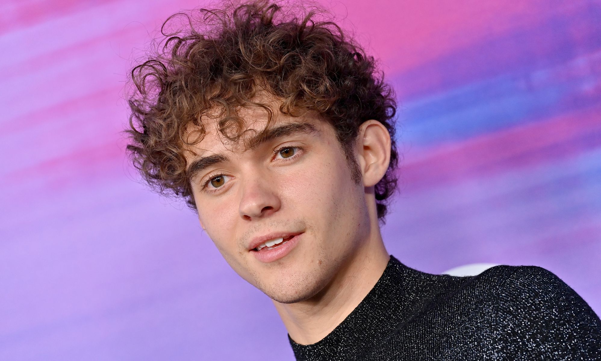 Joshua Bassett in front of a blue, pink and purple background.