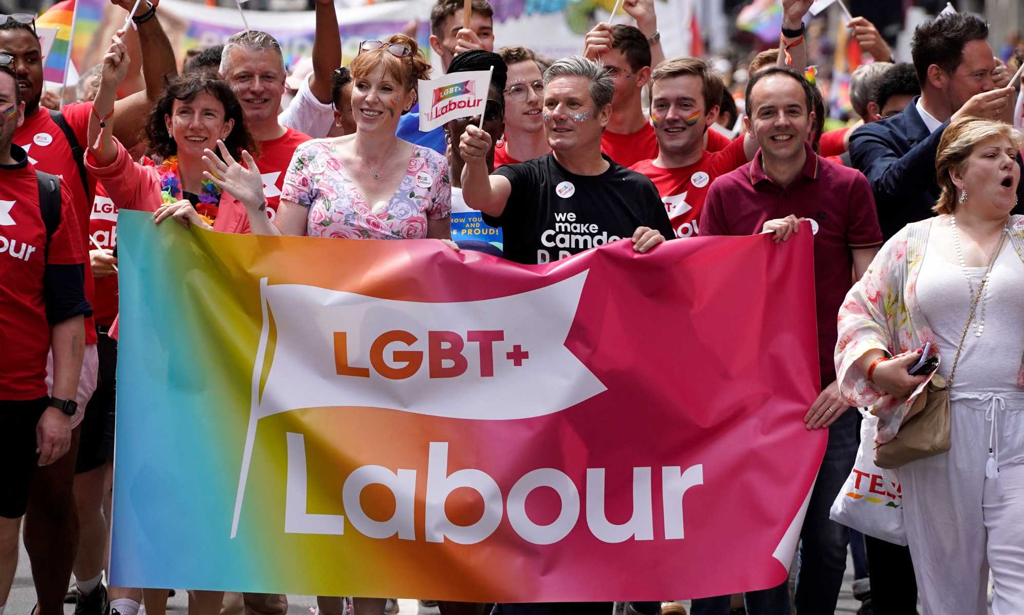 A photo showing LGBT+ Labour at Pride marching amongst a large crowd as they hold a banner that says &quot;LGBT+ Labour&quot;