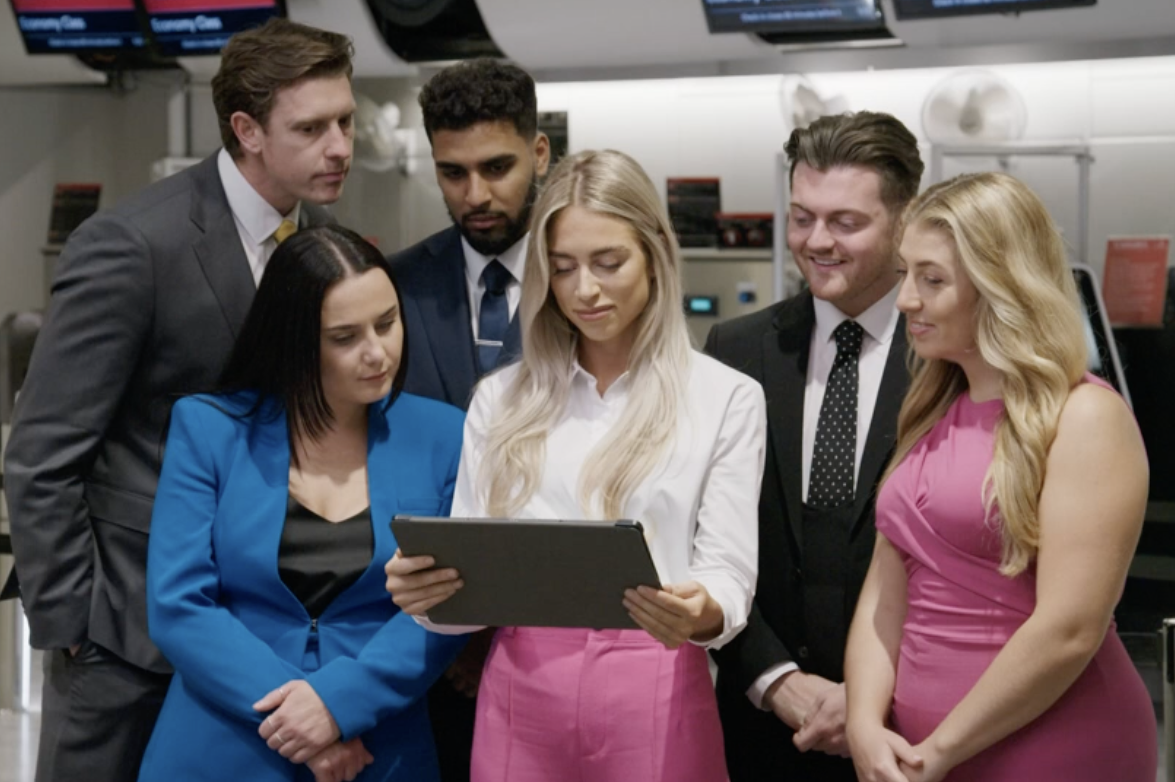 Candidates on The Apprentice crowd around an iPad