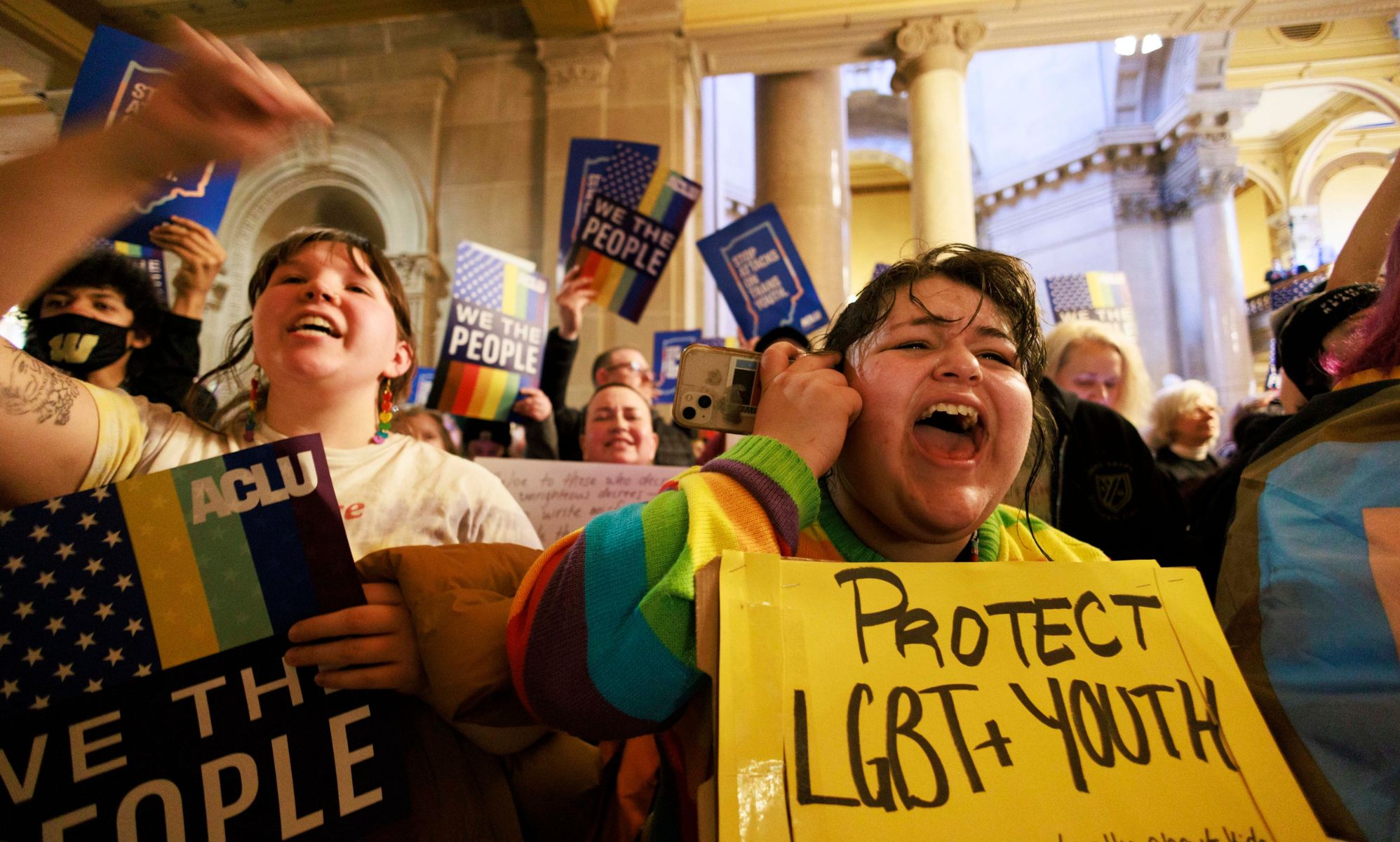 A crowd of people hold up signs in support of the LGBTQ+ community as they gather to protest Indiana state legislature considering a 