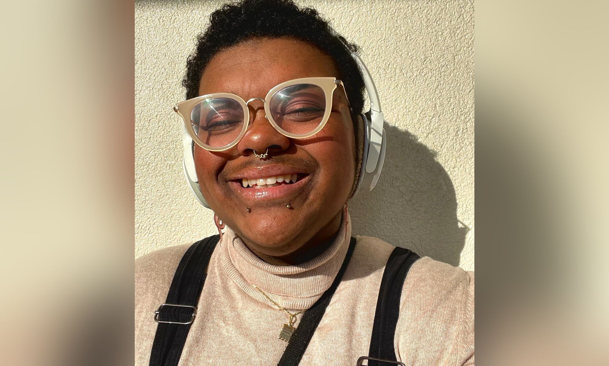 Elliot Kwabena Akosa, an ambassador for LGBTQ+ youth charity Just Like Us, smiles as he poses for a photo while wearing a tan/cream turtleneck top
