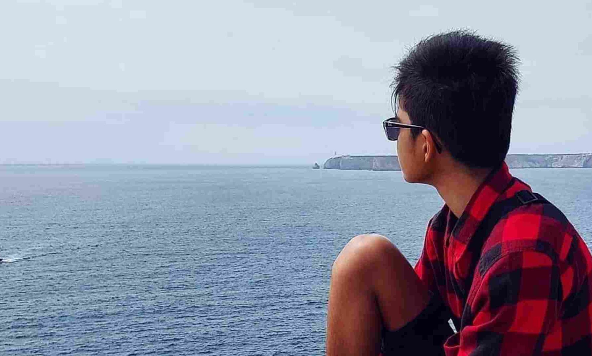 Rayyan Aboobaker, an ambassador for LGBTQ+ youth charity Just Like Us, wears a red and black plaid shirt as he sits with his back to the camera