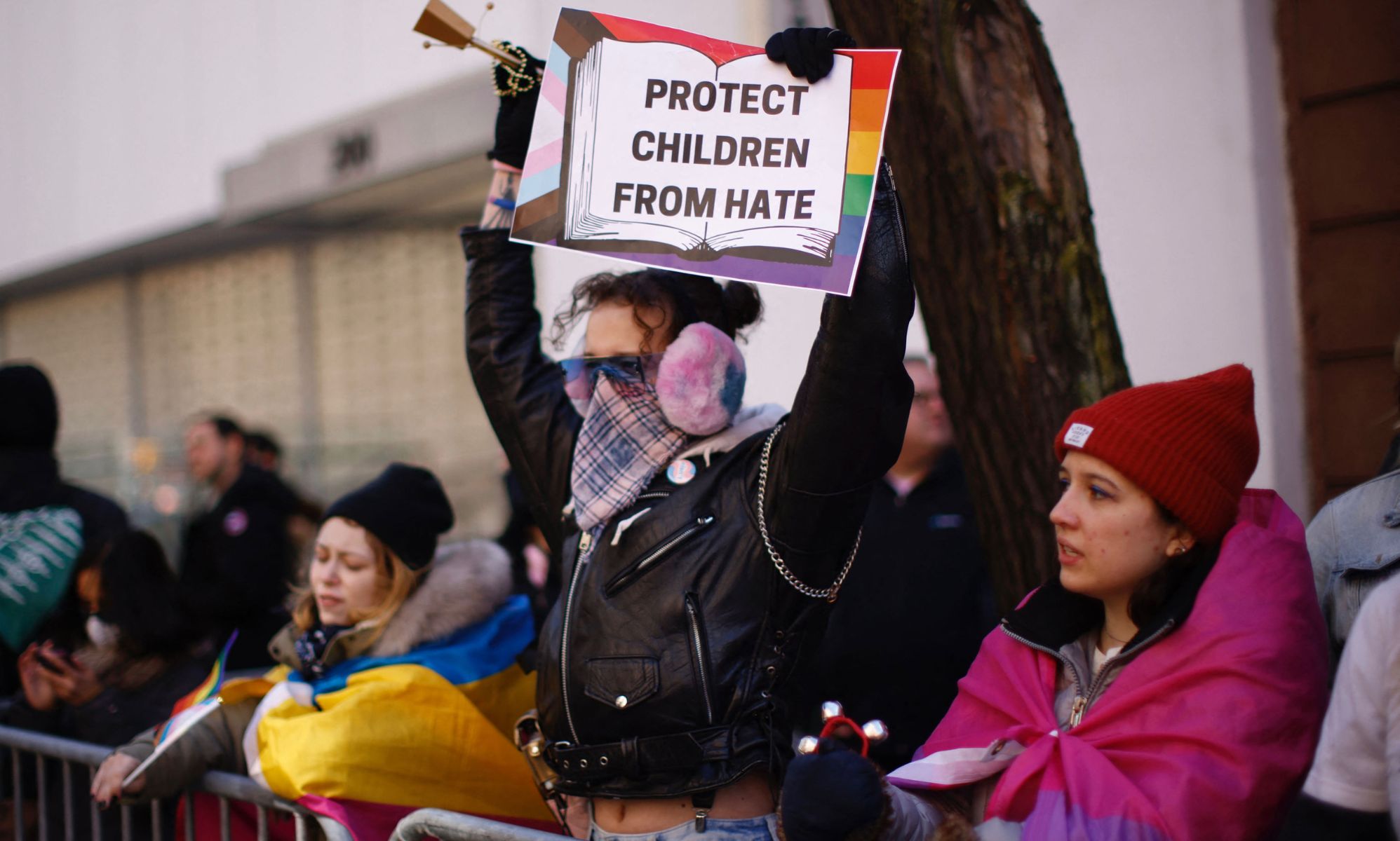 A person holds up a sign that reads &quot;Protect children from hate&quot; with a graphic of the Progressive Pride flag amid a crowd of LGBTQ+ people and allies counter-protesting against hate towards a drag event