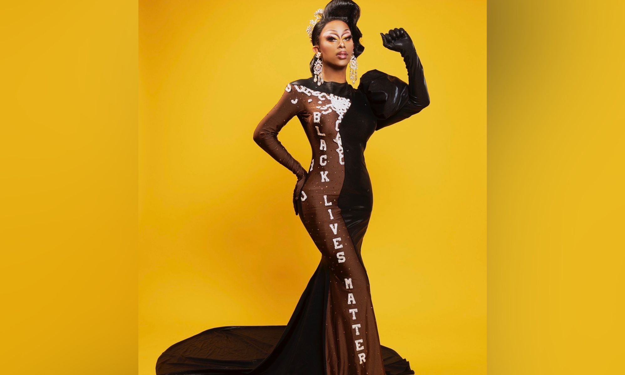 Texas-based drag queen Kylee Ohara Fatale poses with one arm raised up while wearing a black and brown dress with the words 