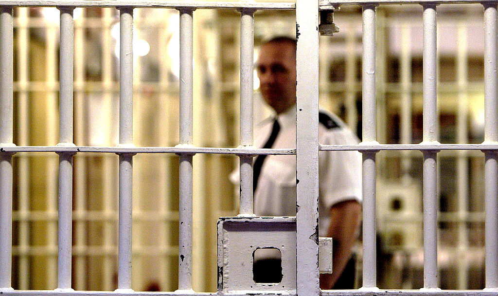 A prison guard at Pentonville Prison stands behind a locked gate.