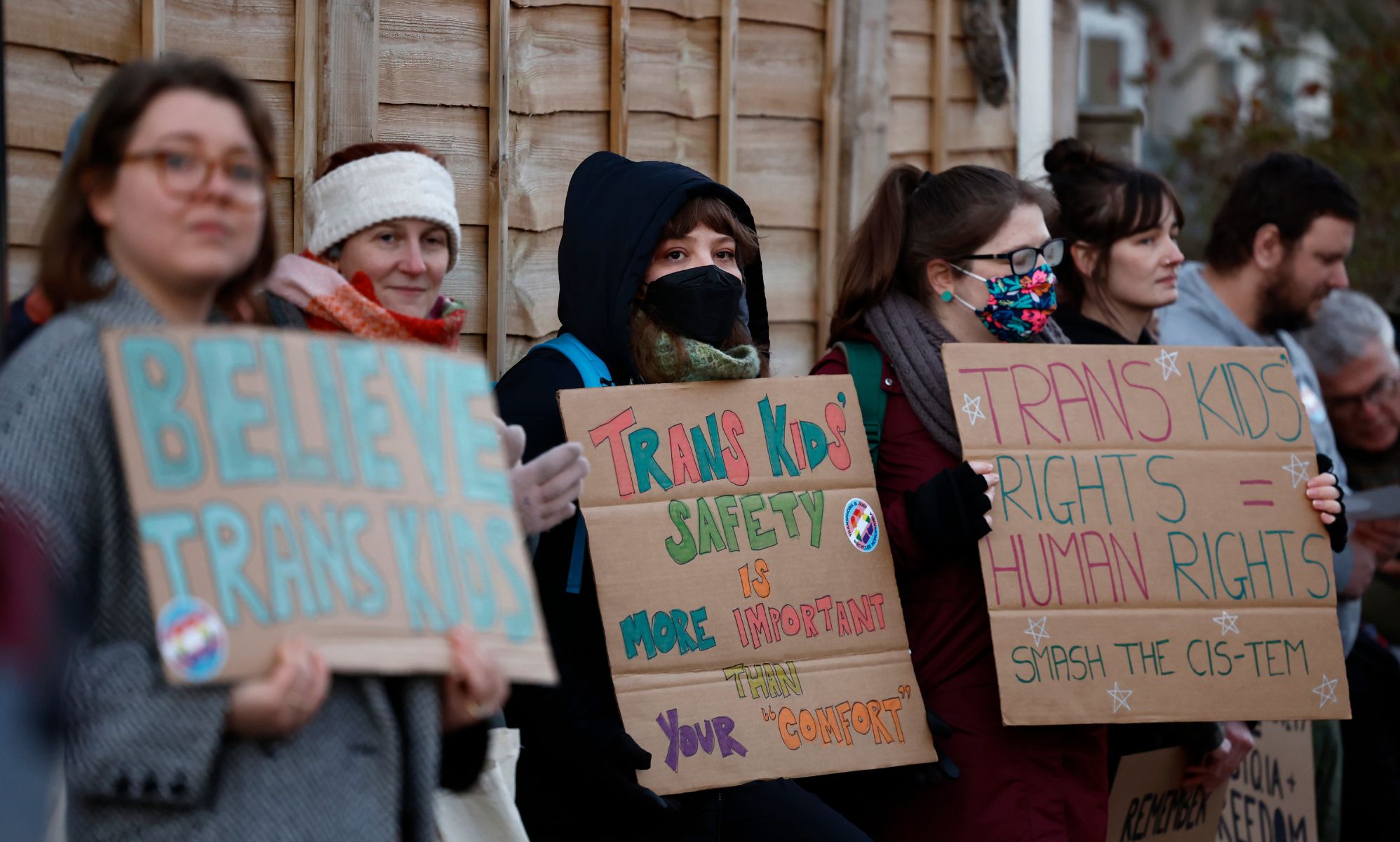 Trans people and allies joyfully protest against anti-trans hate in Scotland by holding up signs in support of the trans community