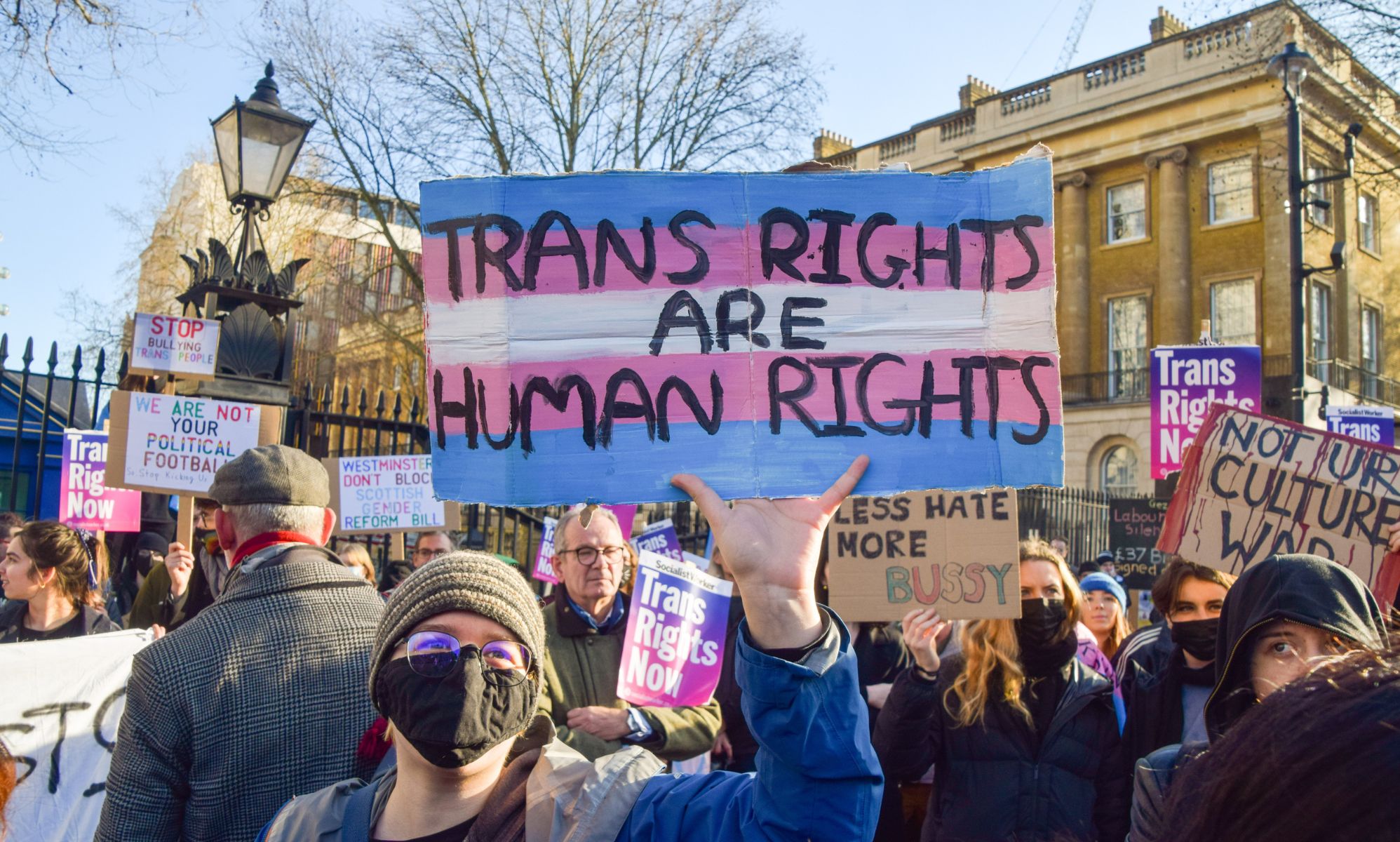 A person holds up a sign in the colours of the trans pride flag (blue, pink and white) with the words 