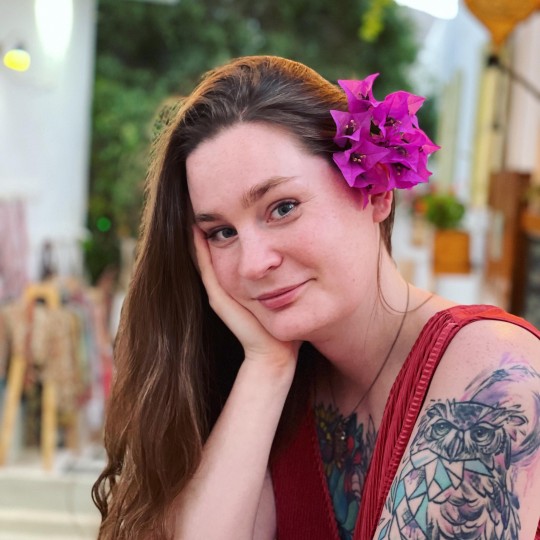 Owl Fisher posing with a pink flower in their hair.