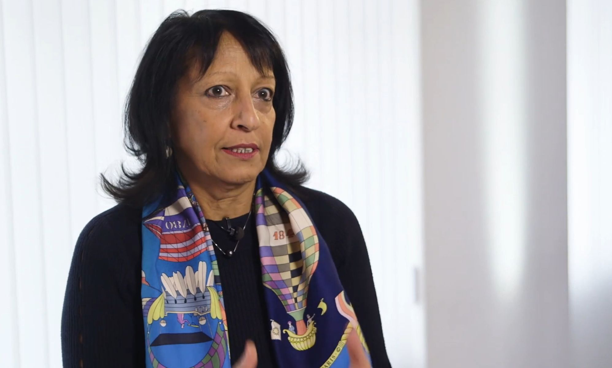 Kishwer Falkner, wearing a multi-coloured scarf, speaks in a white room.