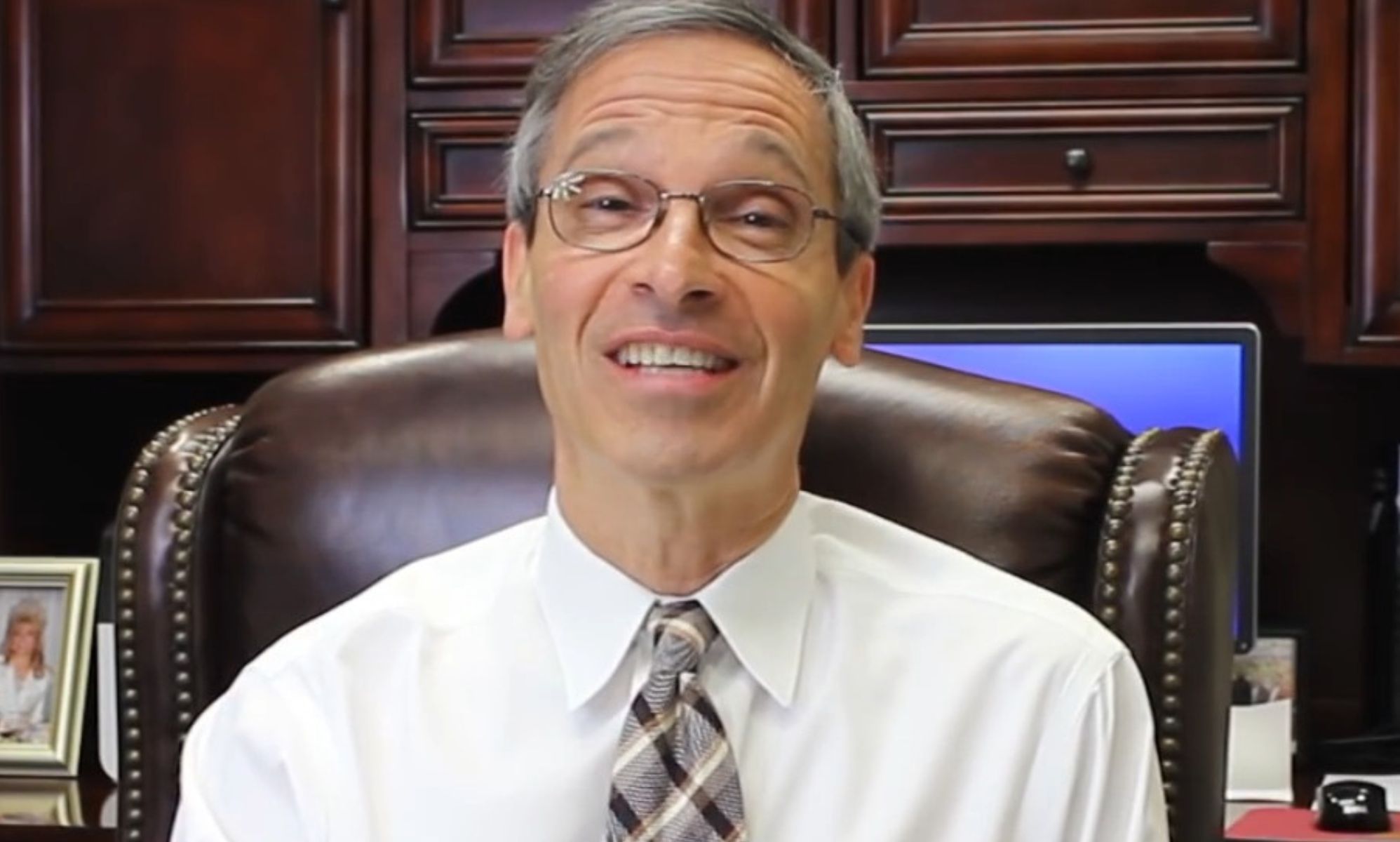 Republican senator Fred Mills, sitting at his desk and smiling while wearing a white button shirt and grey tie.