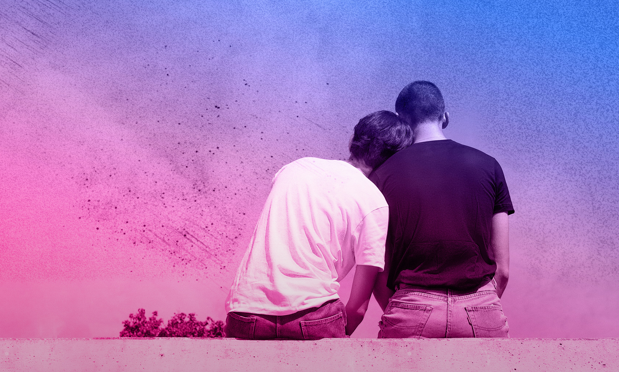 A same-sex couple sitting on a wall facing away from the camera, as one rests their head on the other