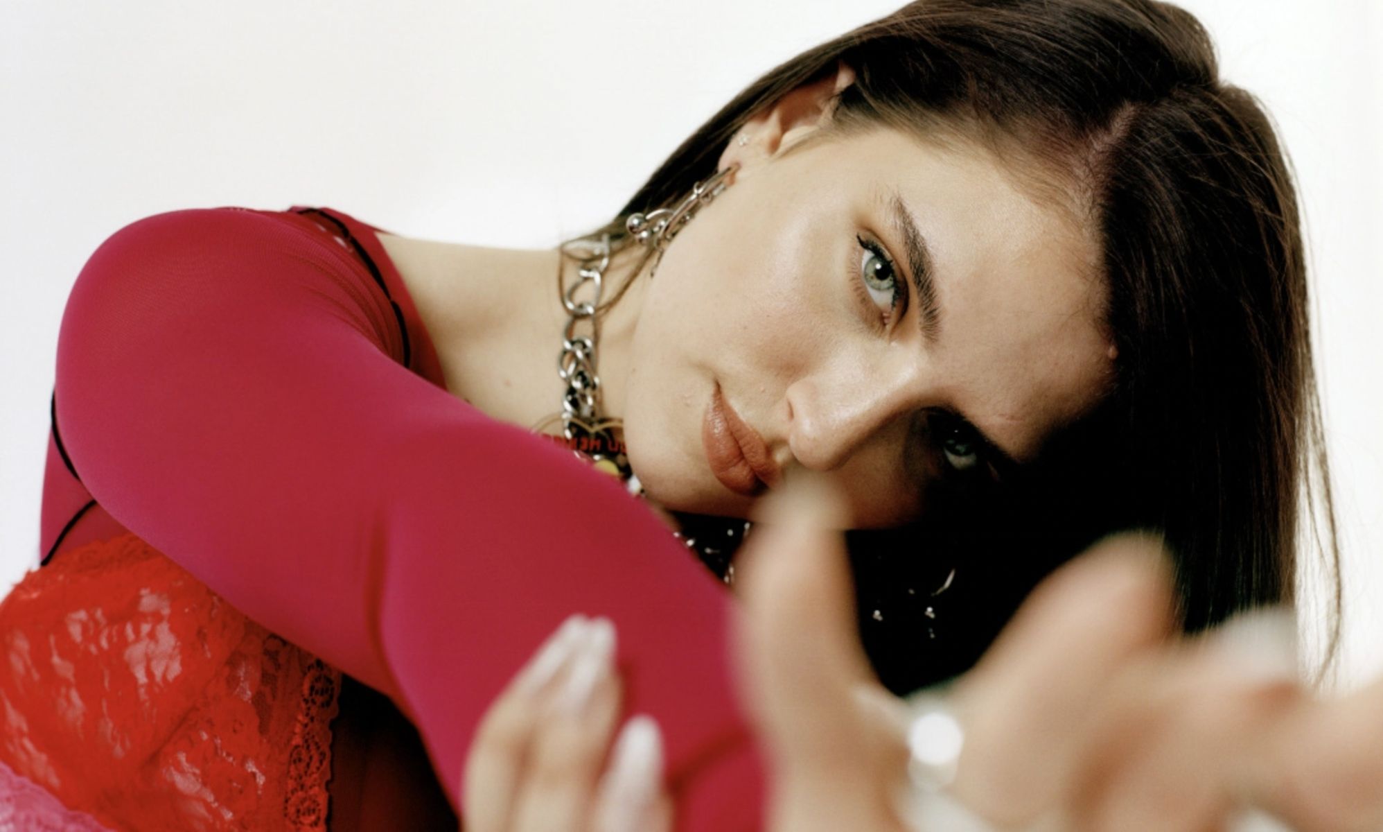 Eurovision 2023 UK entrant Mae Muller in a red top and gold necklase with her hand touching the camera.