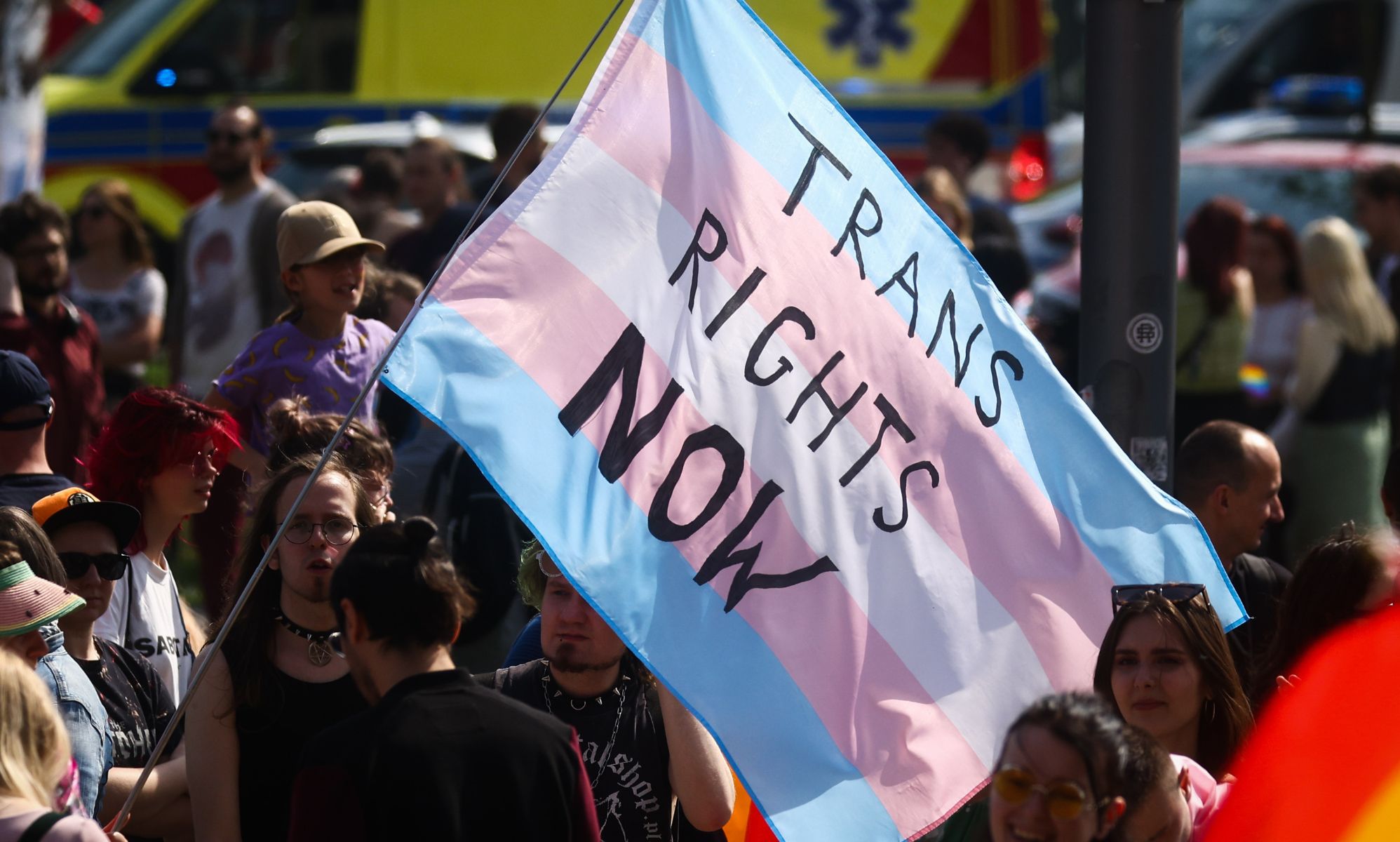 A person holds a giant trans flag that reads 