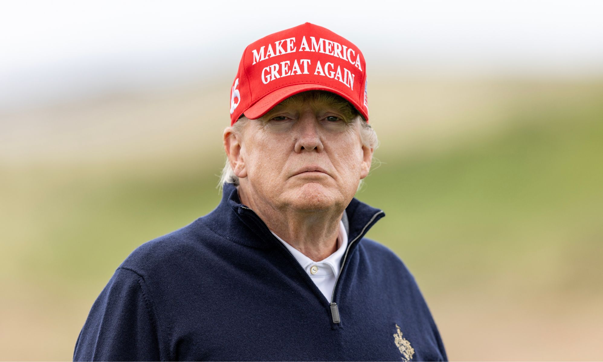 Former President Donald Trump, who is running as a 2024 Republican presidential candidate, wears a white shirt, blue jacket and red hate with his slogan 